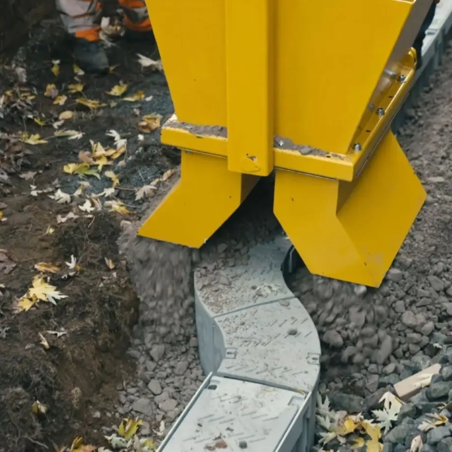 Baumaschine füllt Schotter in eine Rinne mit Betonplatten.